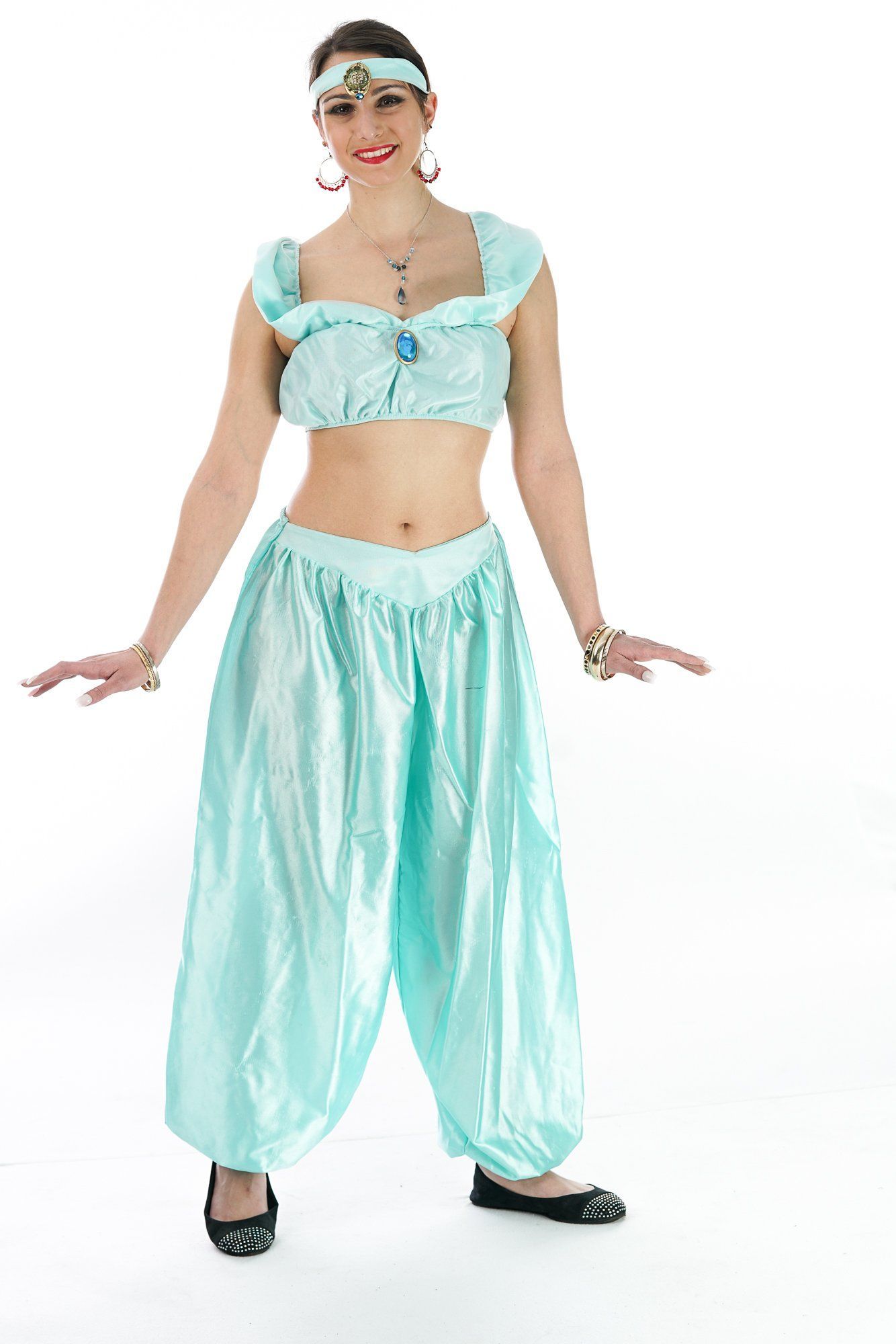 Woman in a turquoise costume with harem pants and cropped top, standing and smiling against a white background