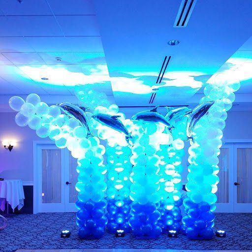 Blue and white balloon arch with dolphins in a banquet hall, lit by cool blue ceiling lights