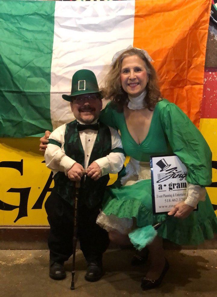 Two people posing in St. Patrick’s Day costumes before an Irish flag backdrop
