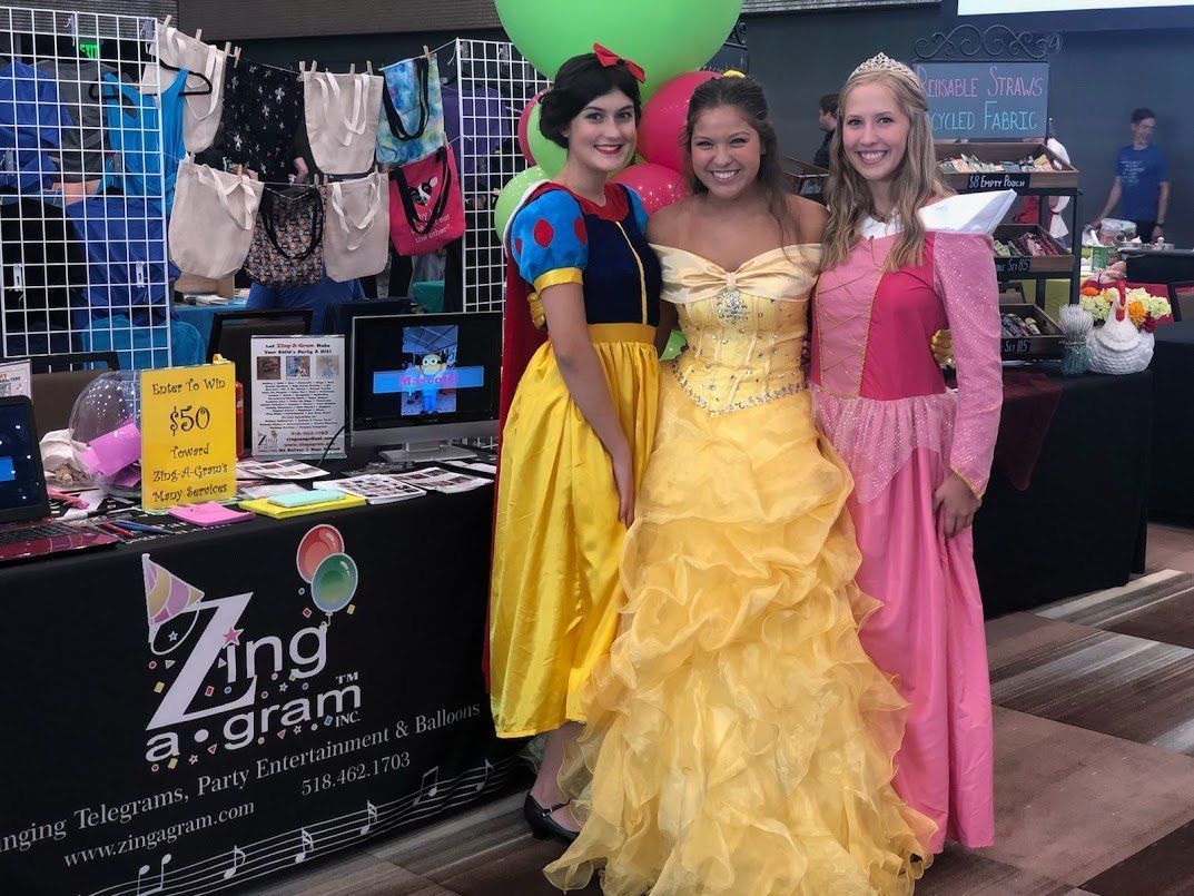 Three women in princess costumes posing at a booth with dresses and accessories