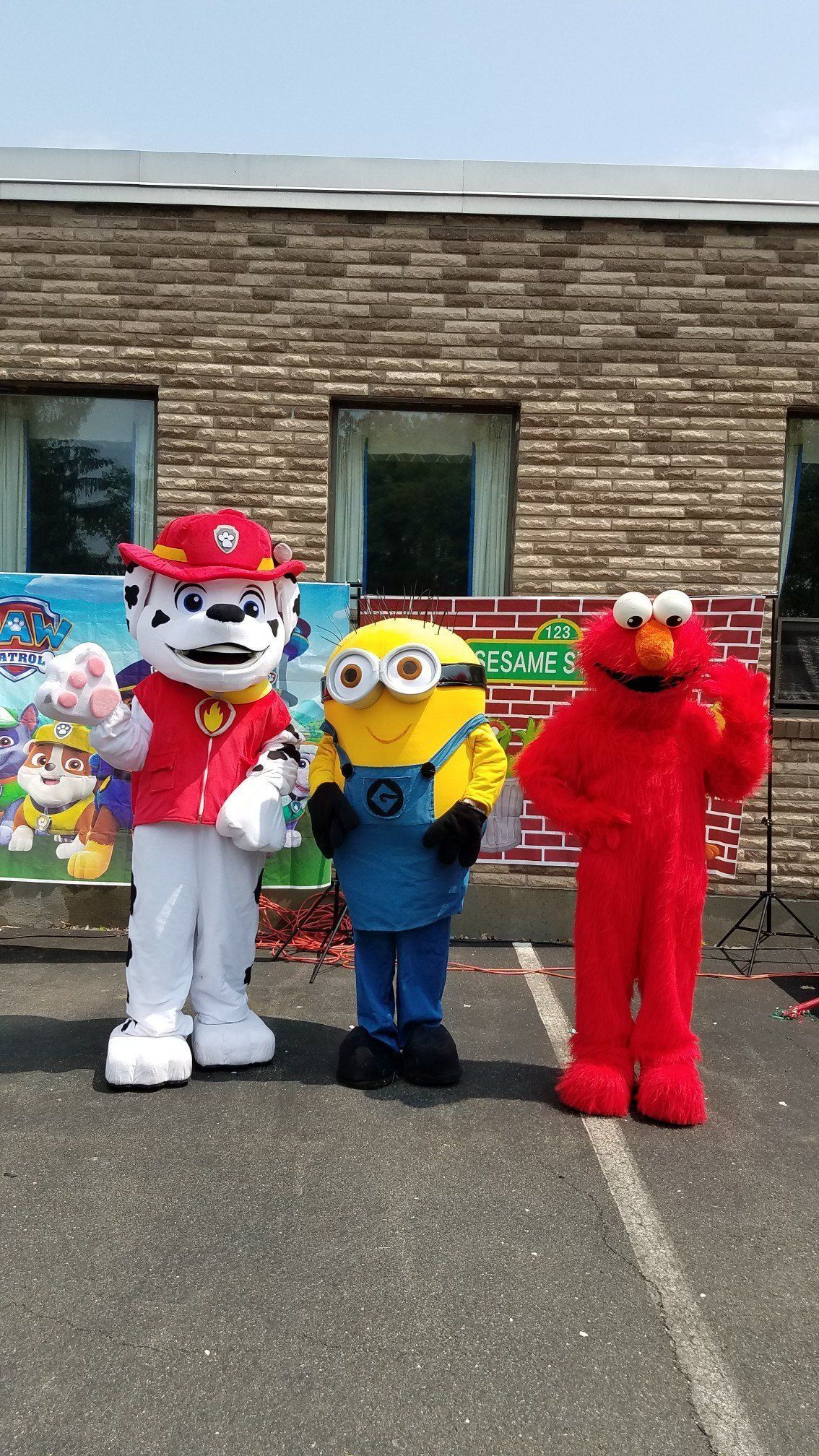 Three costumed mascots standing together outdoors in front of a brick building.