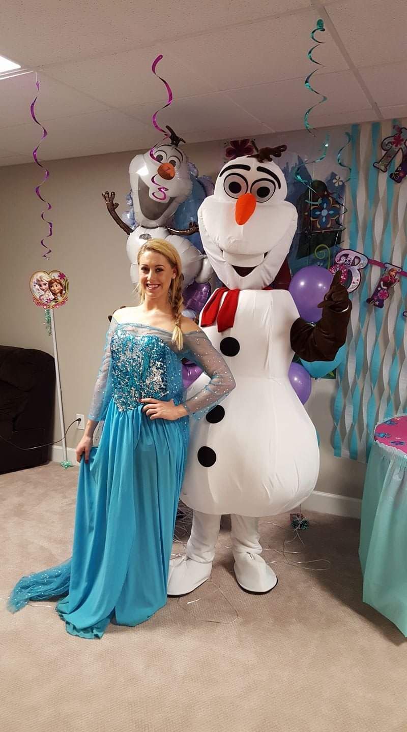 Woman in a blue gown posing beside a large Olaf character at a decorated indoor party.