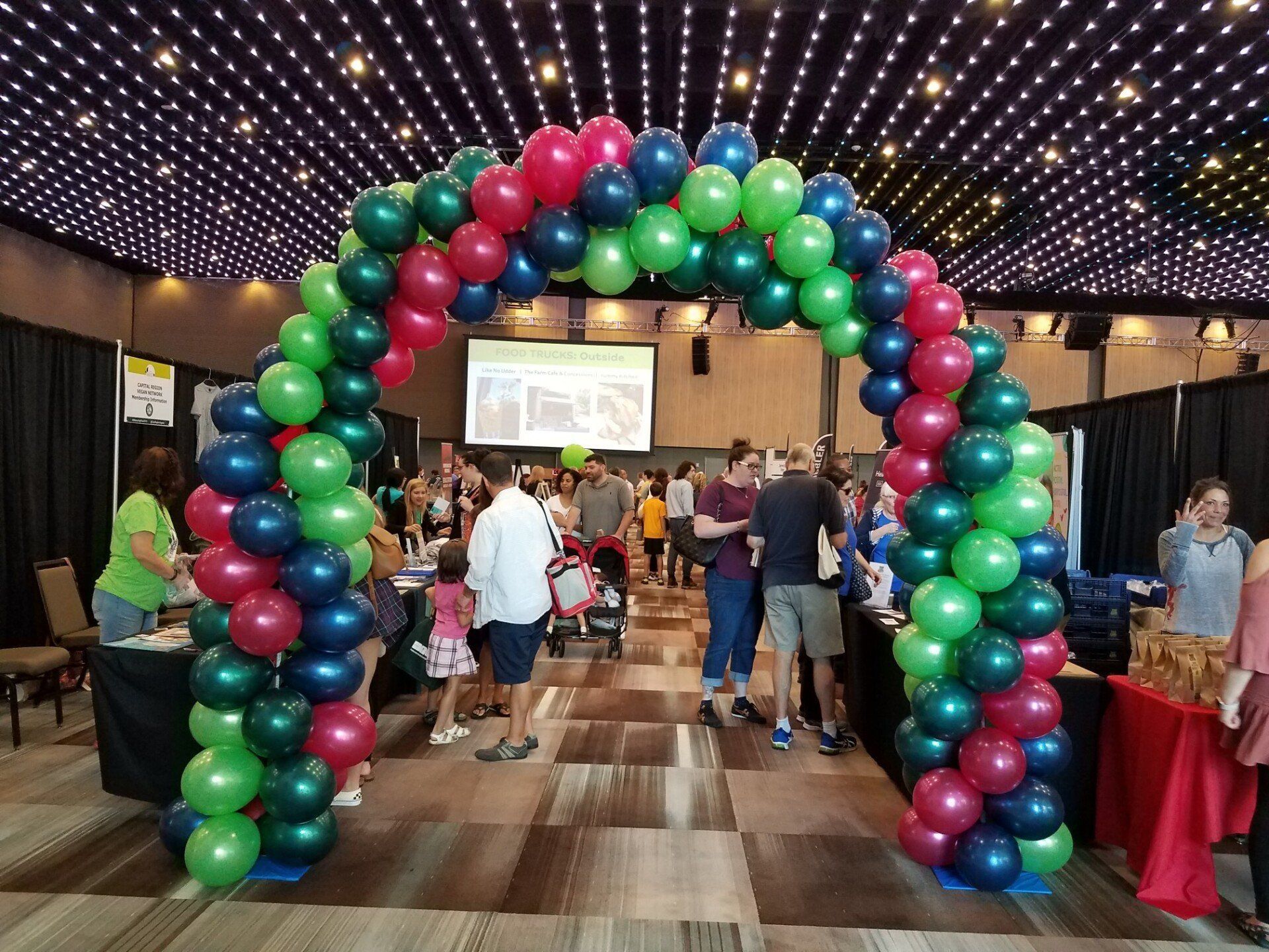 Balloon arch in a conference hall with people gathered beneath it and a presentation screen in back