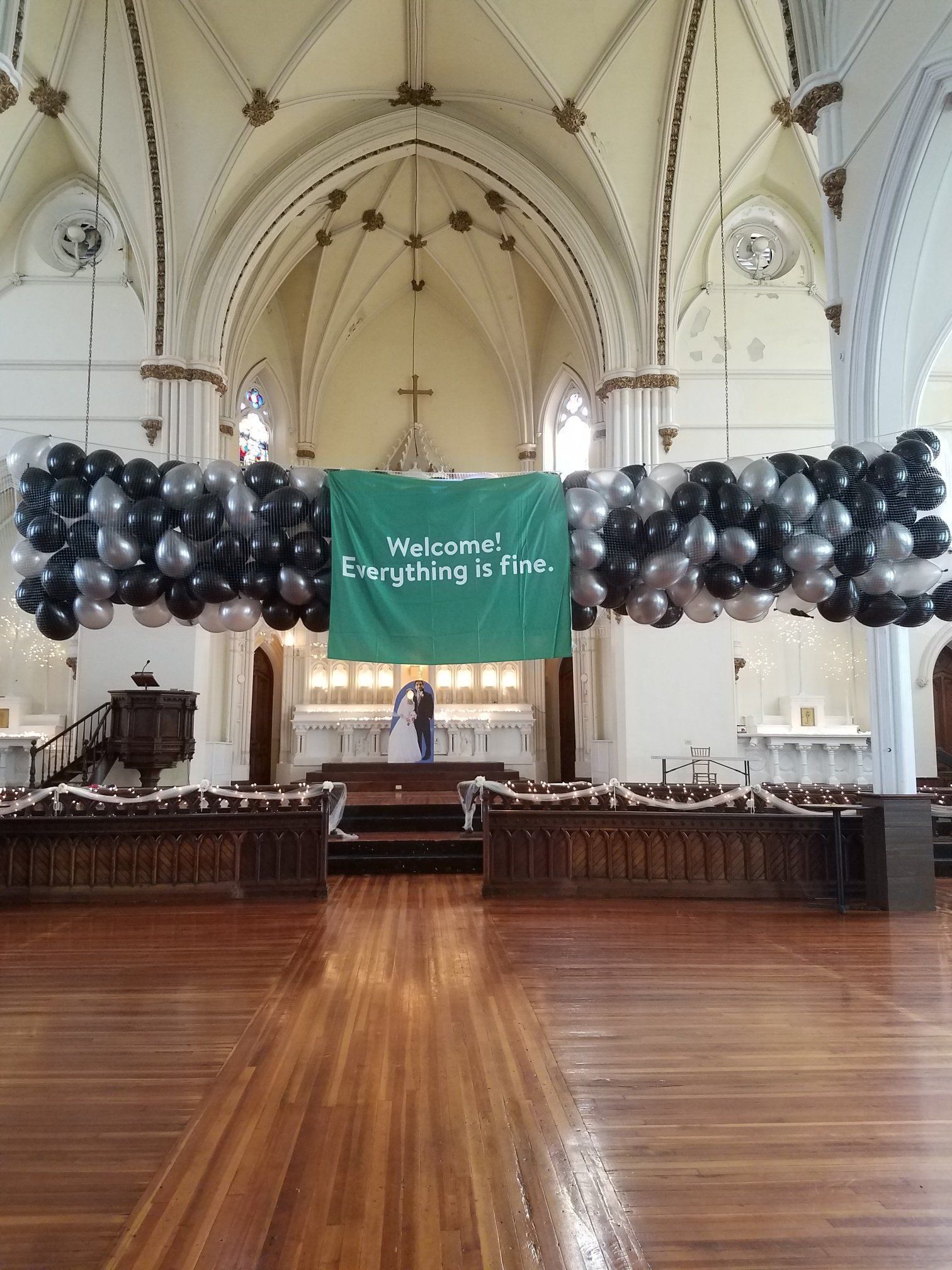 Church interior with black balloon arch and green “We come in peace” banner across the altar area