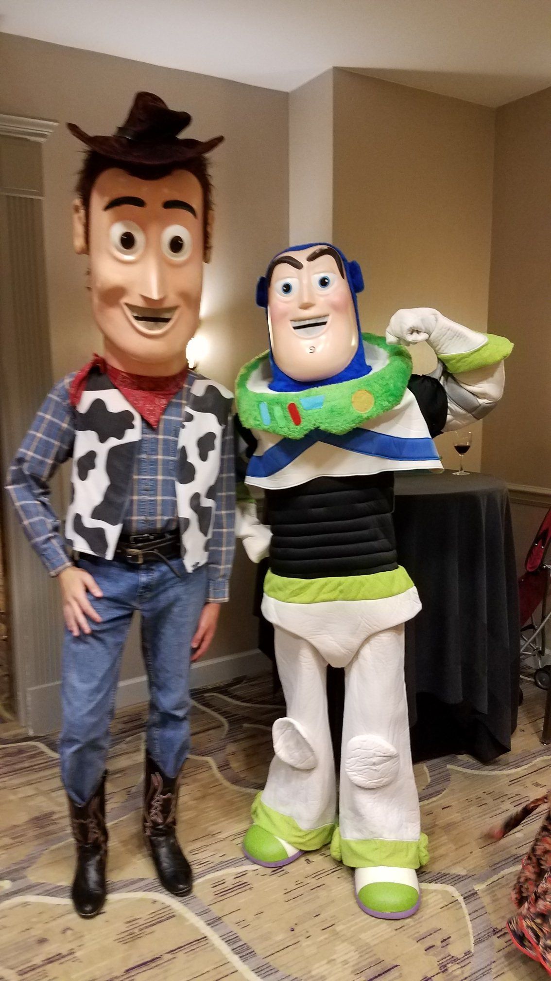 Toy Story characters Woody and Buzz Lightyear standing together indoors at a costume event.