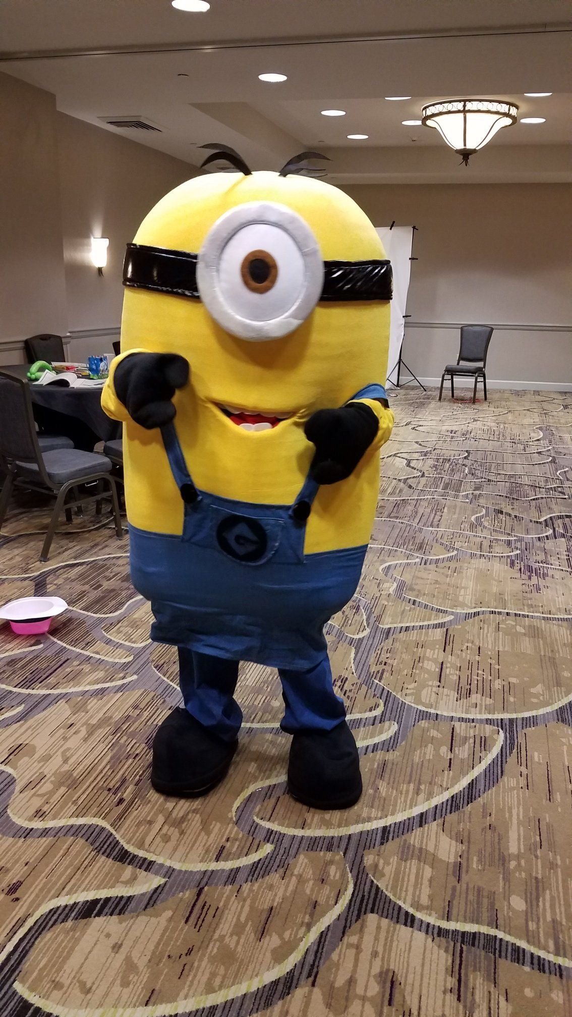 Person in a yellow Minion costume posing in a hotel ballroom.