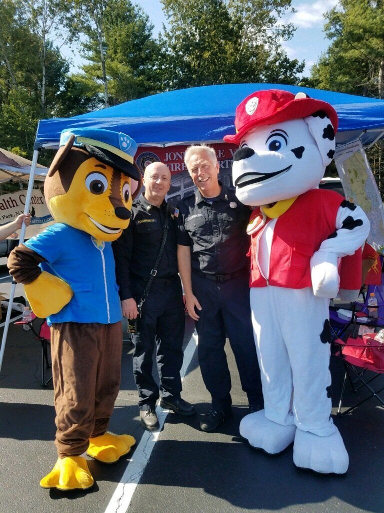 Two costumed dog mascots and a man posing outdoors under a blue canopy.