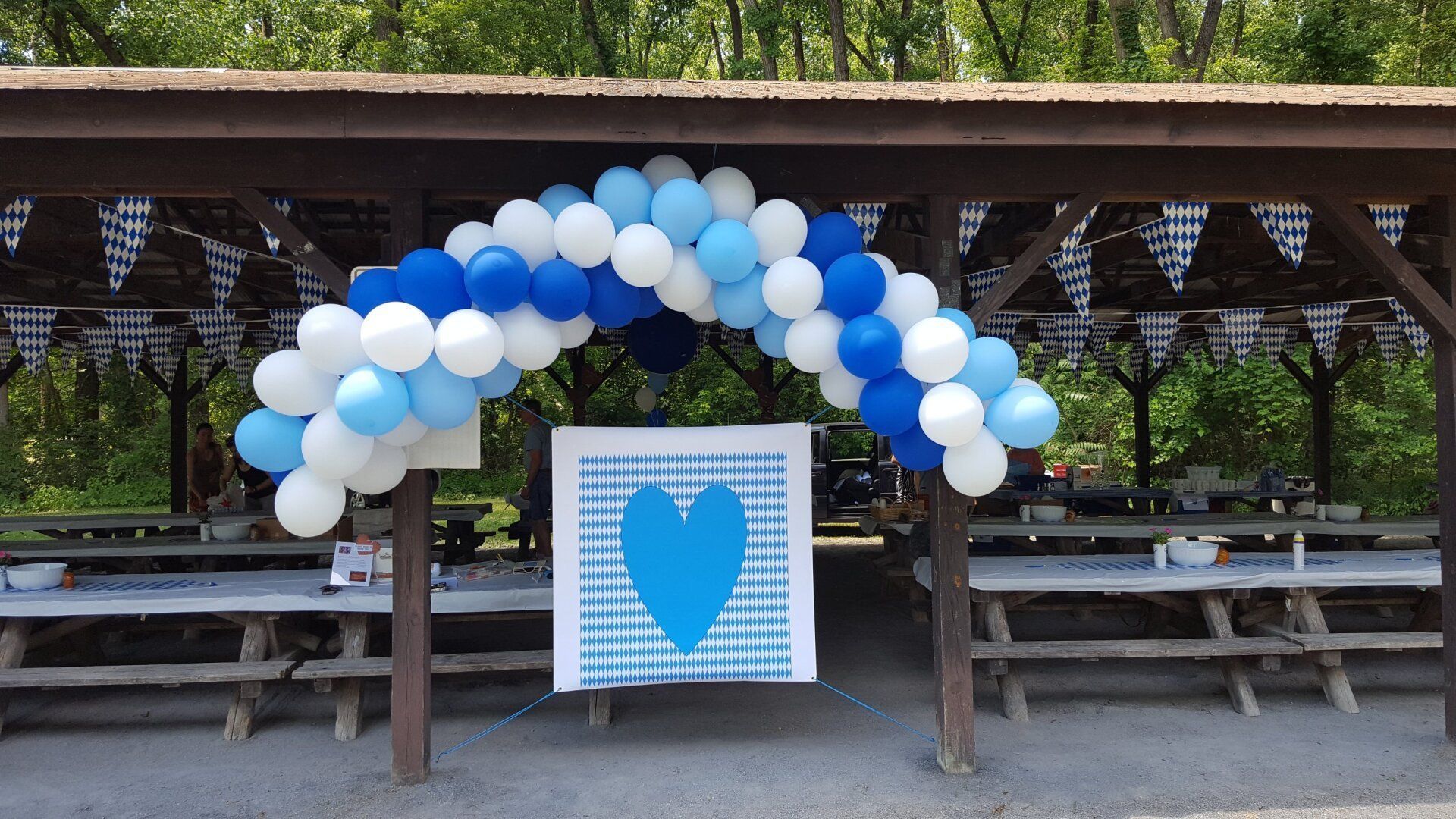 Blue and white balloon arch over a picnic shelter with a blue heart sign centered below