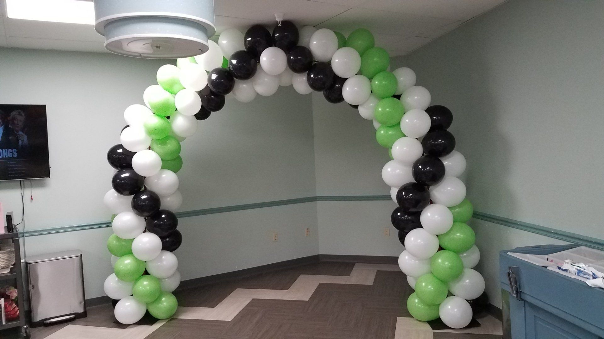 Black, white, and green balloon arch in a room hallway at an event or party