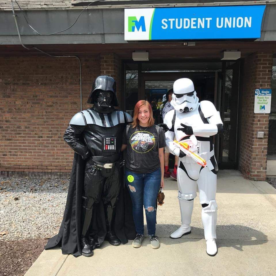 Three people posing outside a student union, two in Darth Vader and Stormtrooper costumes.