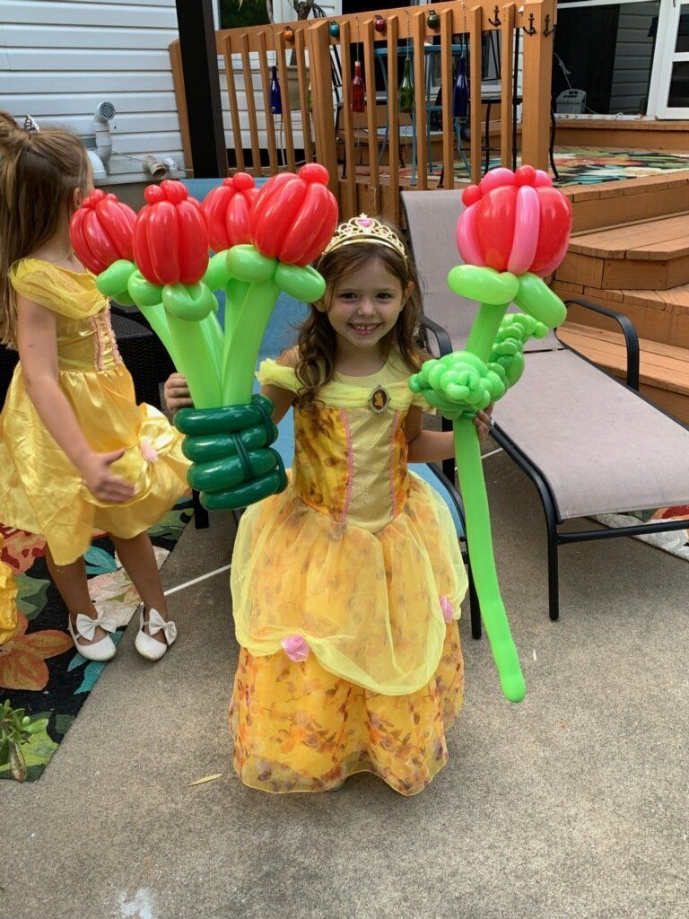 Child in yellow dress holding giant red flower balloons on a patio, with another child nearby.