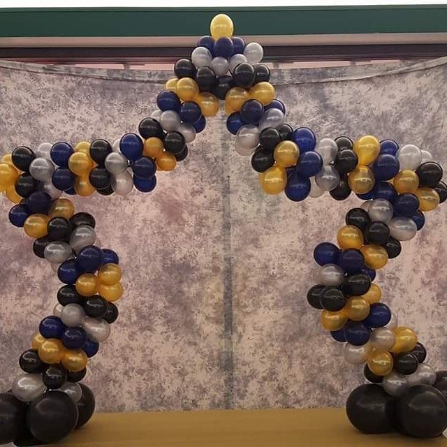 Balloon arch in black, gold, and navy forming a star-like entrance against a mottled gray backdrop.
