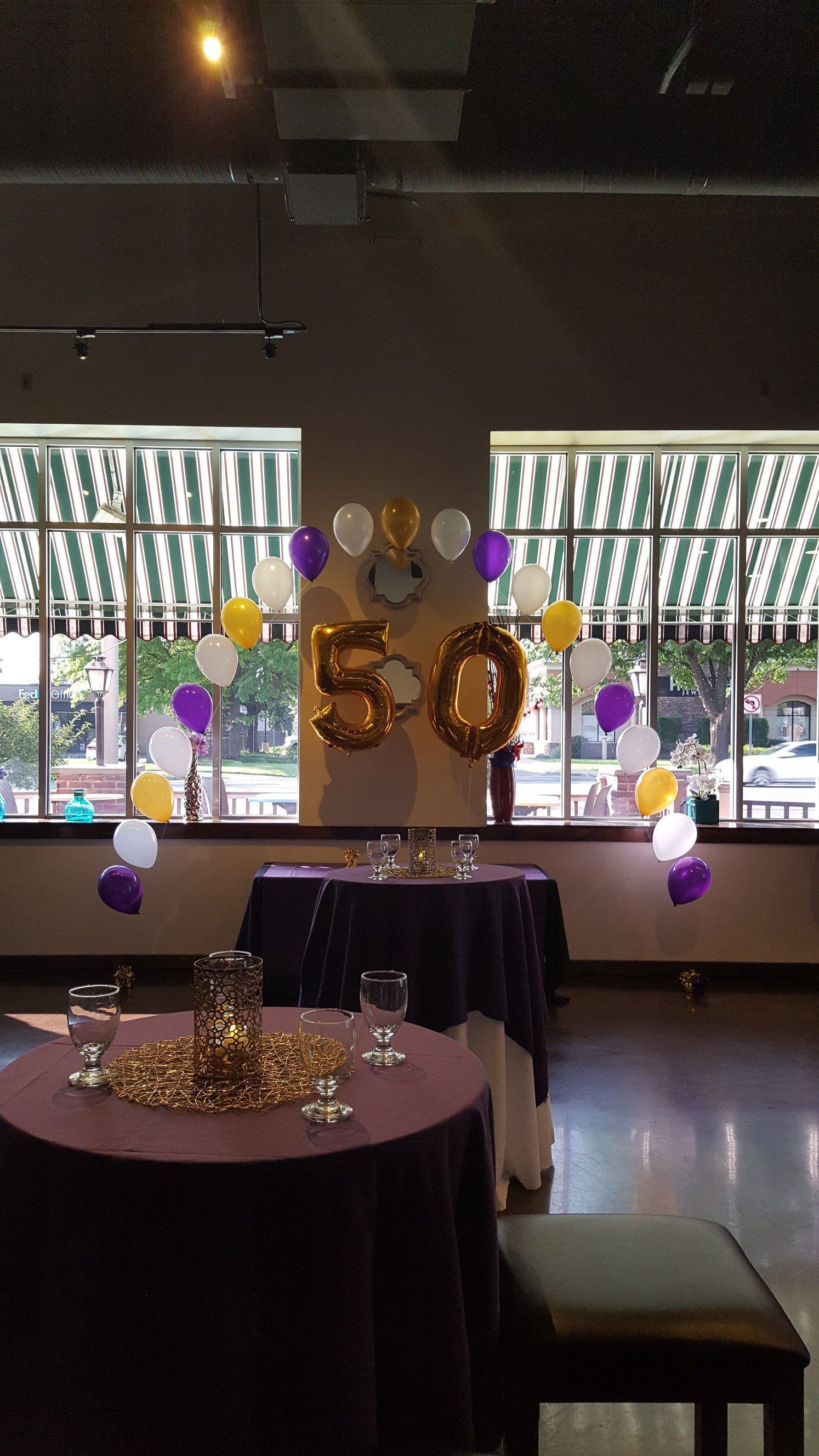 Decorated event hall with a balloon backdrop, purple and gold accents, and round tables set for a celebration
