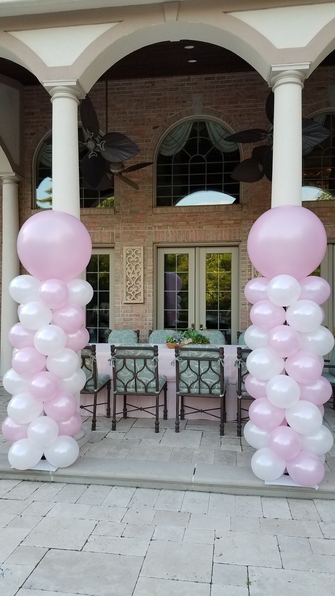Pink balloon columns framing an arched outdoor patio entrance with tables and chairs inside