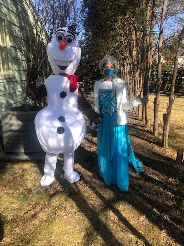 Person in a snowman costume and woman in a blue gown standing outdoors in a sunny yard.