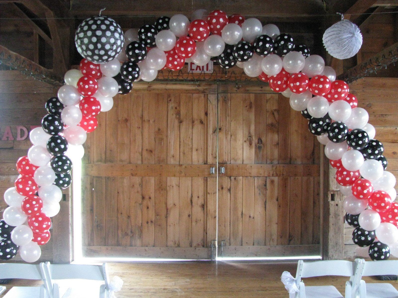 Red, black, and white balloon arch framing wooden double doors at an event entrance