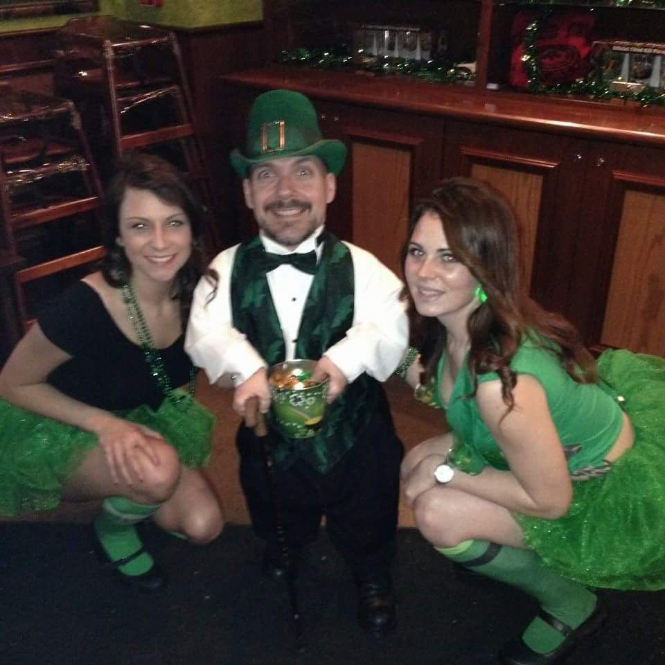 Three people in green St. Patrick’s Day outfits posing together in a bar.