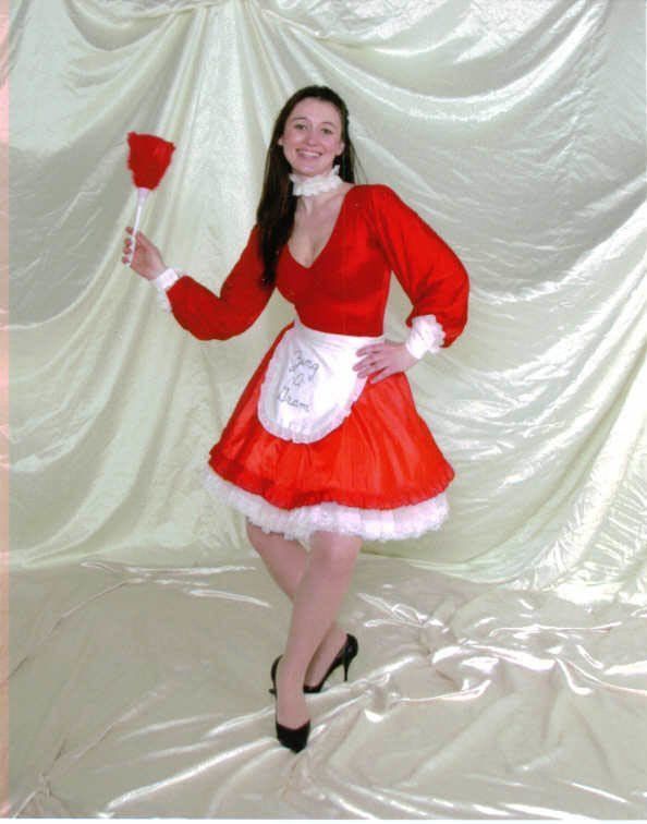 Person in a red-and-white festive dress holding a small red prop against a draped backdrop.