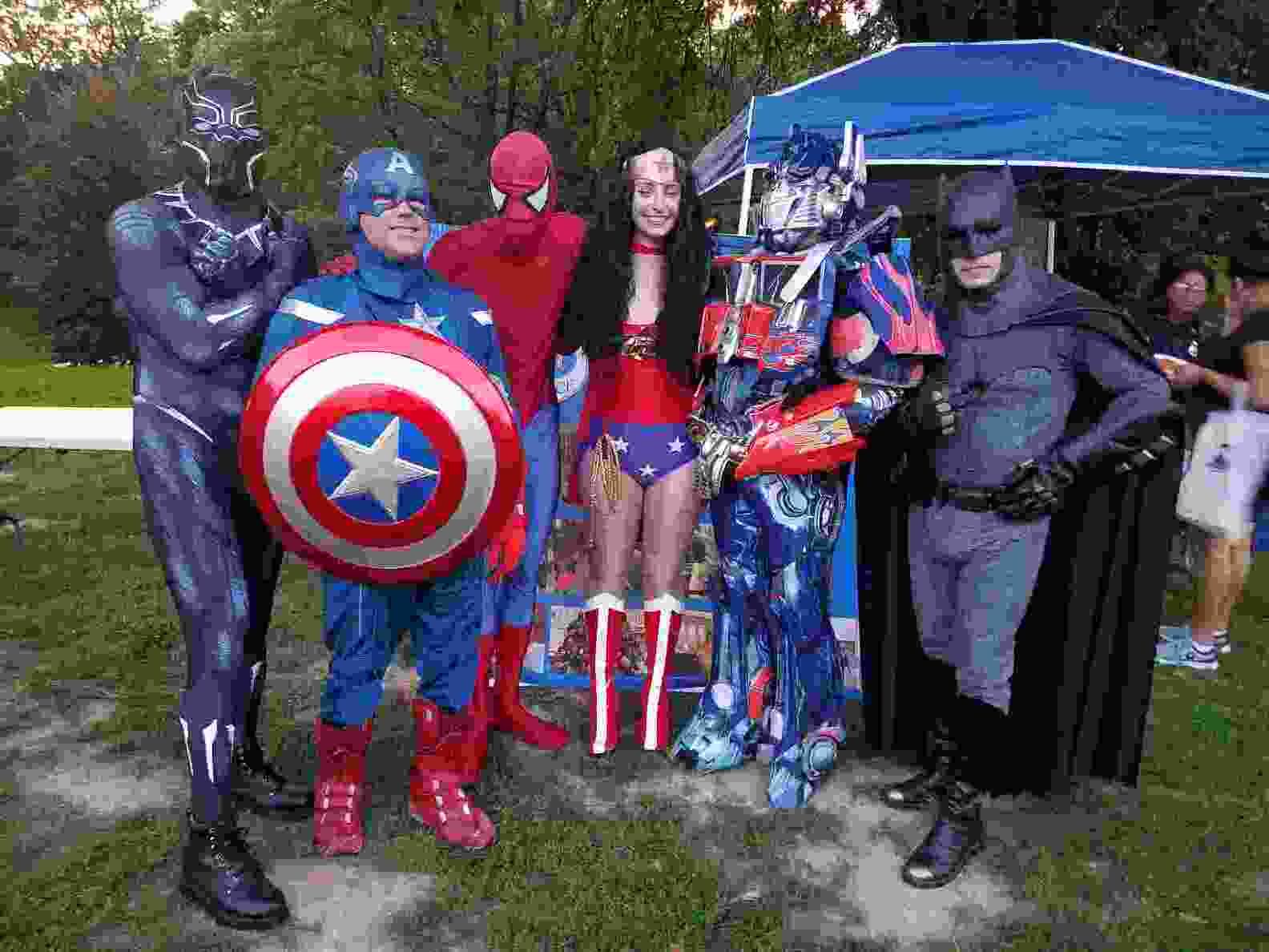 Group of costumed superheroes posing outdoors, including Captain America, Spider-Man, and Batman.