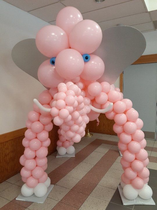 Pink balloon arch and bear-like figure with white ears in an indoor hallway under a ceiling.