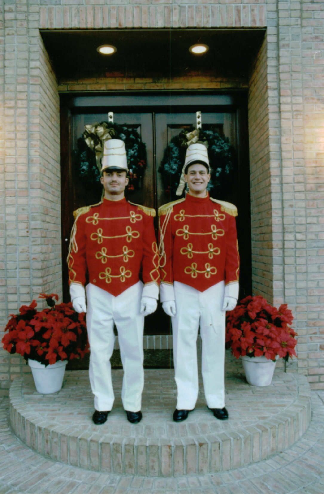 Two uniformed guards standing at a brick entrance with red potted flowers