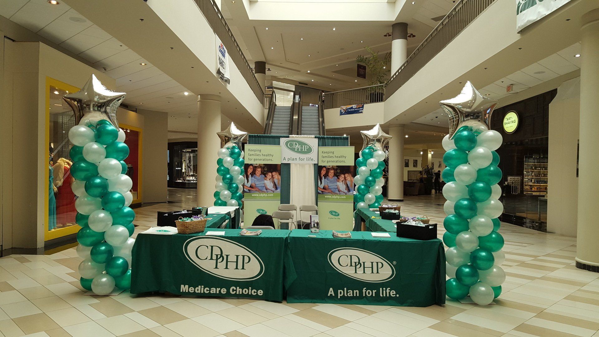 Green and teal balloon-decorated CIPH booth in a mall atrium, with tables and signage