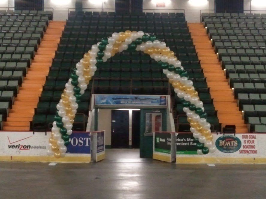 Indoor arena entrance with white-and-green balloon arch and empty green bleachers behind it