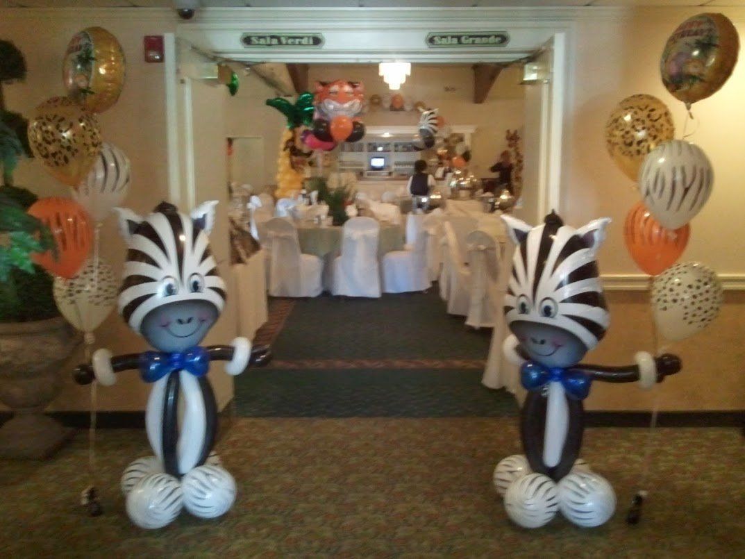 Two zebra balloons framing a decorated party entrance with white chairs and gold balloons
