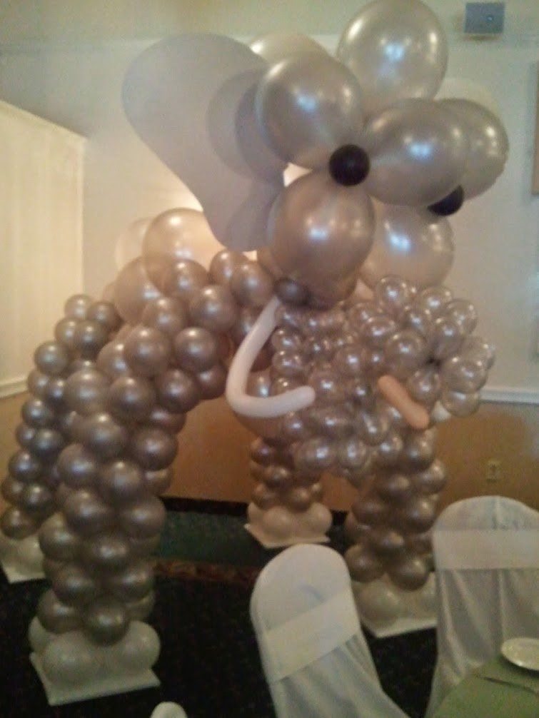 Balloon sculpture of a poodle-like dog with a flower-shaped head in a room, made of metallic silver balloons