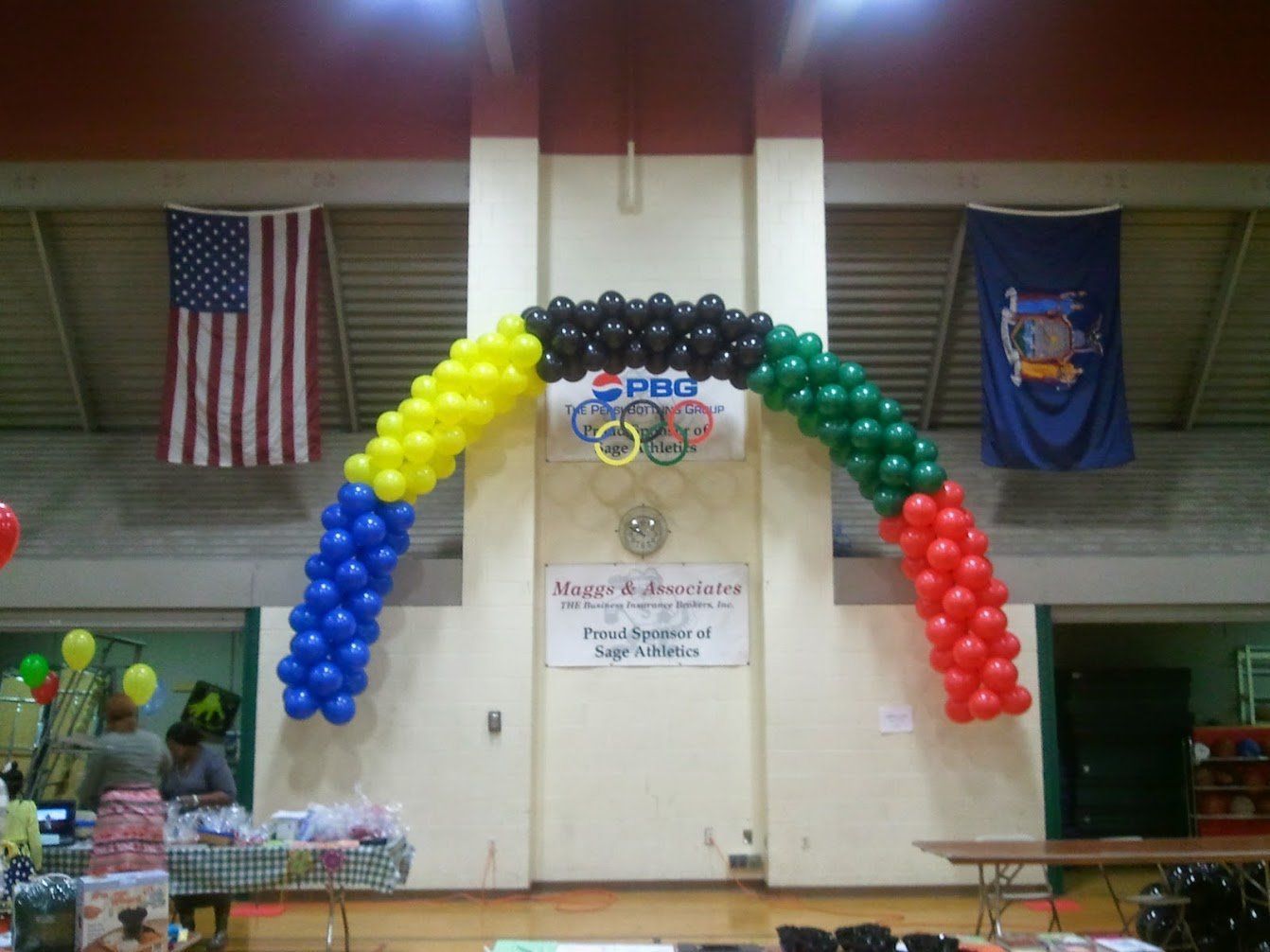 Balloon arch in red, yellow, blue, and black on a stage with U.S. and Florida flags in the background