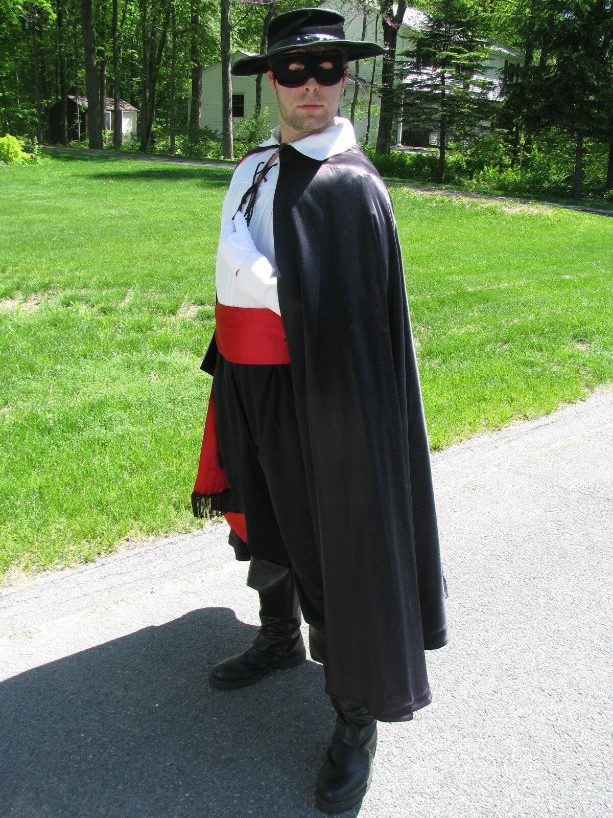 Person in a black hat and cape standing outdoors on a sunny path