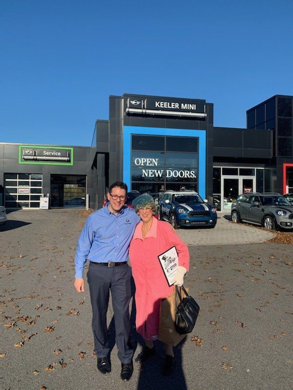 Two people standing outside a building with an “OPEN NEW DOORS” sign on a sunny day.