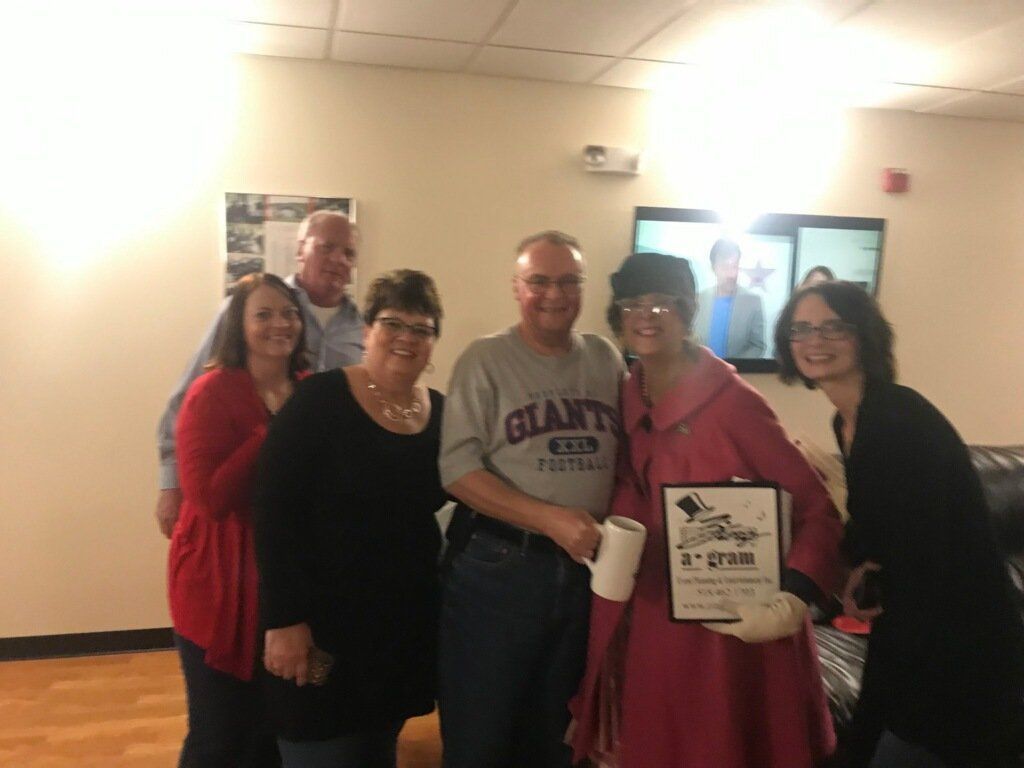 Five people pose indoors, smiling and holding a certificate and plaque.