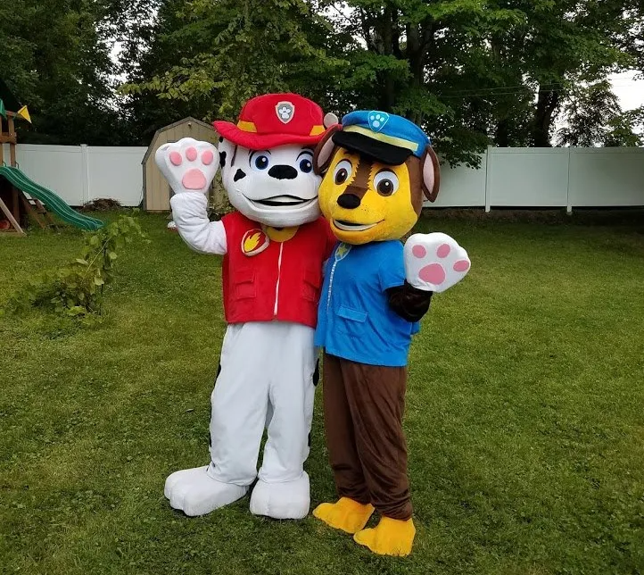 Two Paw Patrol mascots waving on a grassy lawn, one in red and white, one in blue and brown.