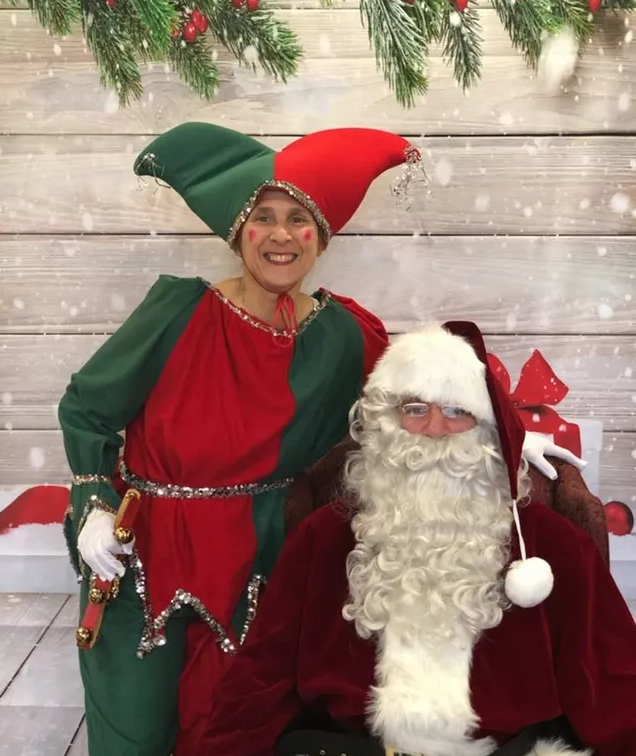 Two holiday performers in red and green costumes posing in front of a snowy backdrop