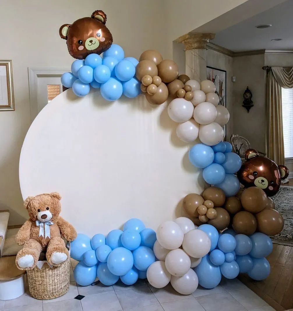 Teddy bear balloon display with a white round backdrop and blue, white, and brown balloons in a living room