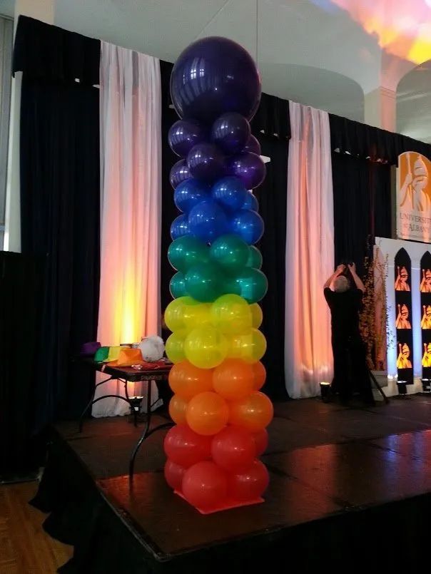 Rainbow balloon column on a stage with black and white drapes and warm lighting