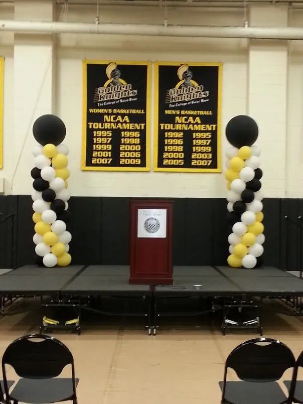 Empty awards stage with black-and-gold balloon columns, podium, and NCAA championship banners.