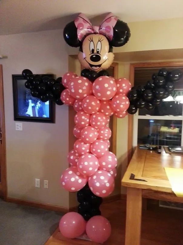 Minnie Mouse balloon sculpture in a living room, made of pink and black balloons with outstretched arms.
