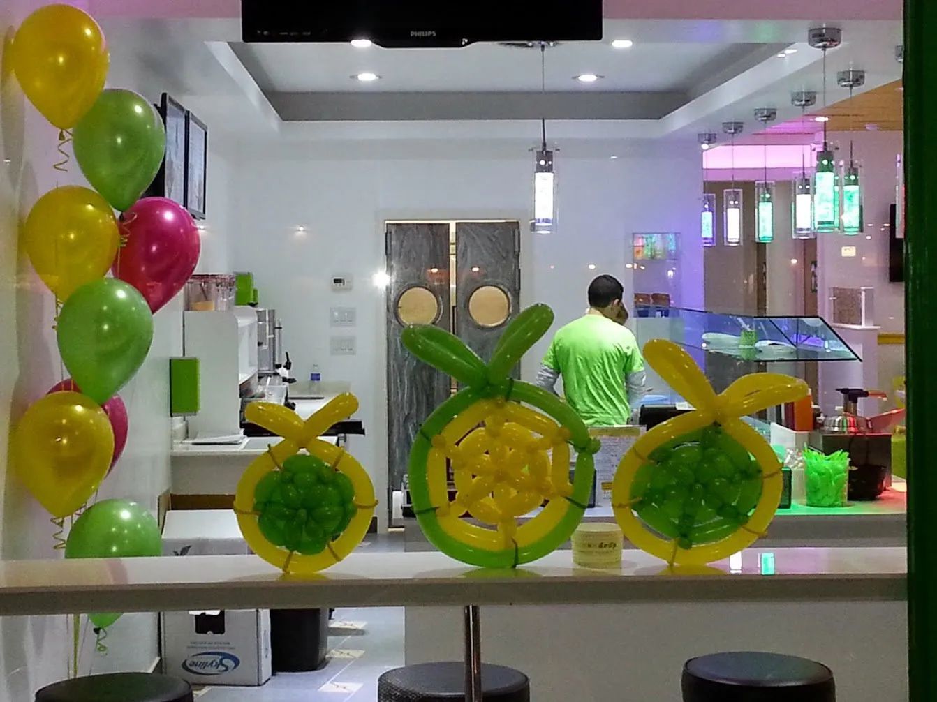 Decorated shop counter with green and yellow balloon arrangements and a person in a green shirt inside