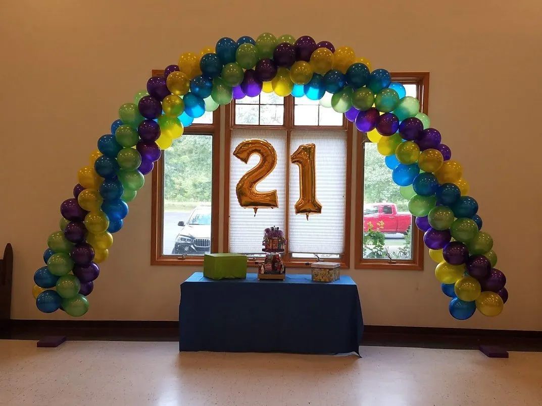 Balloon arch around a window with gold “21” balloons and a table in front