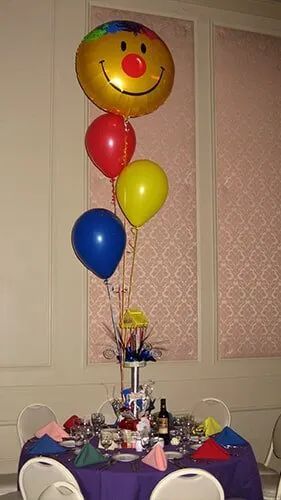 Balloon-decorated table with party favors and a smiling face balloon in a banquet room