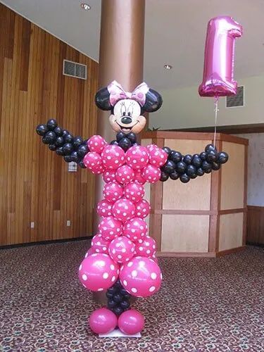 Minnie Mouse balloon sculpture in pink and black, holding a pink number 1 balloon in a hallway