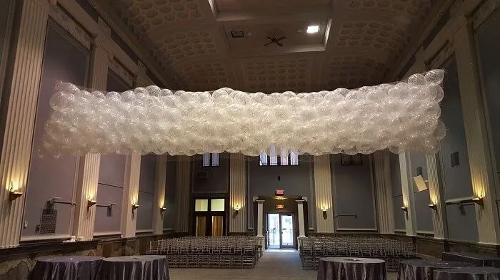Large white balloon canopy suspended across a formal banquet hall with round tables and chandeliers.