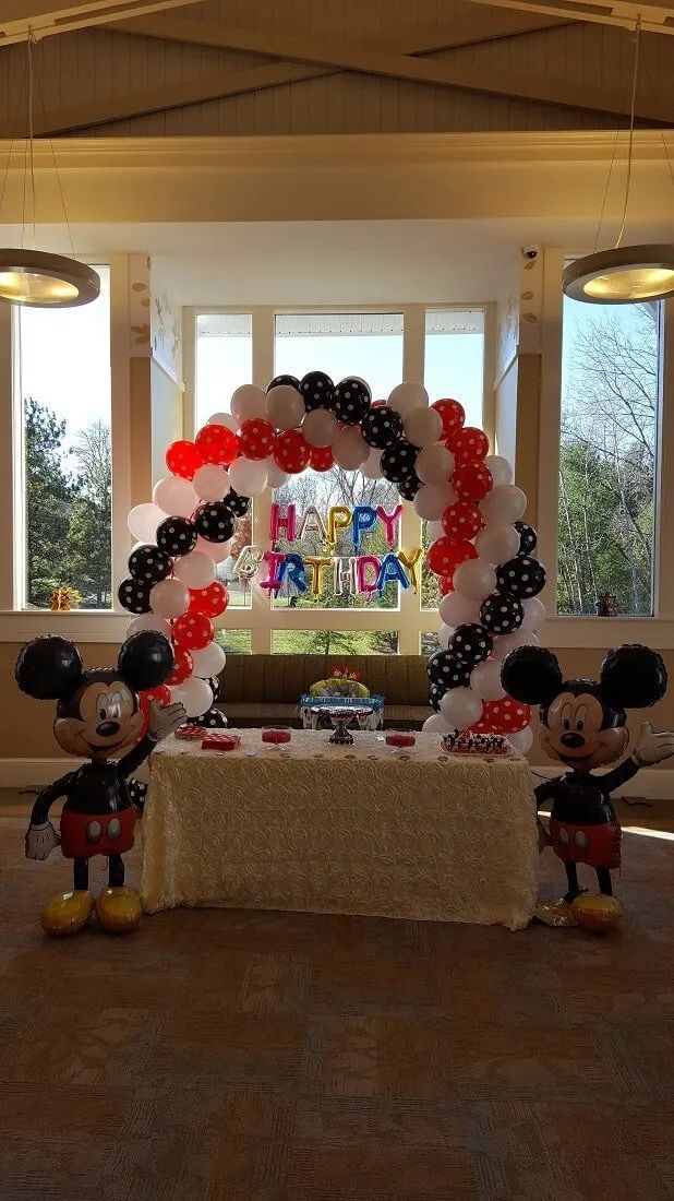 Mickey Mouse balloon arch over a decorated table with two Mickey figures in a bright indoor room
