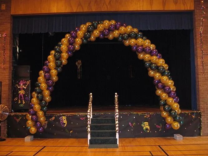 Balloon arch in purple and gold framing a stage with steps and black curtain backdrop
