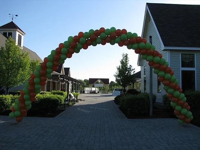 Red and green balloon arch over a paved walkway between residential buildings on a sunny day