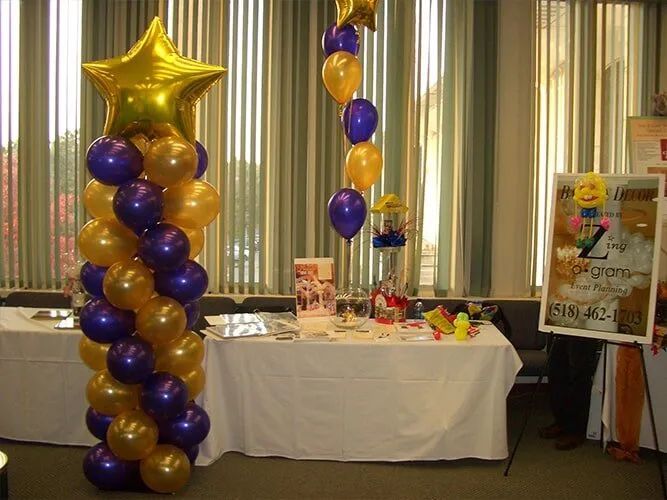 Purple and gold balloon column beside a decorated table at an indoor celebration