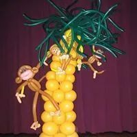 Balloon sculpture of monkeys hanging from a yellow palm tree with green leaves against a purple curtain.