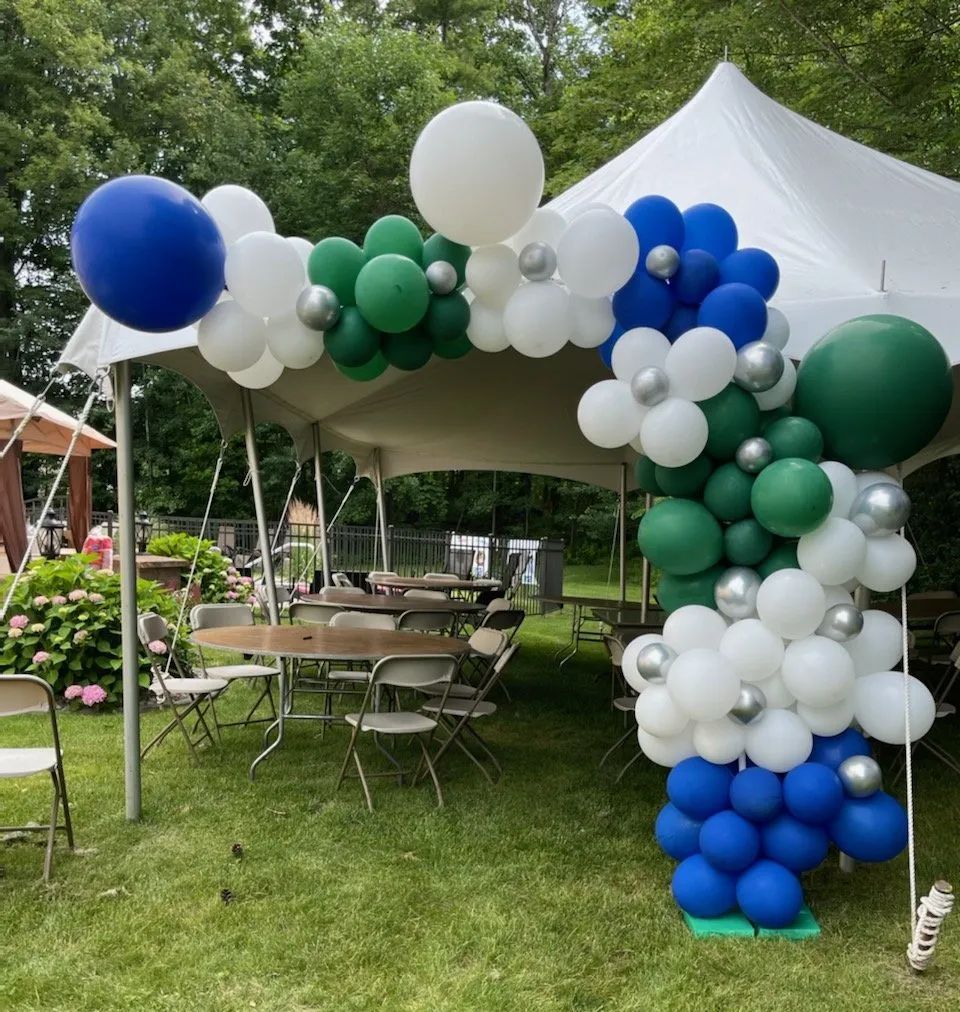 Outdoor party tent decorated with blue, green, and white balloon arches over tables and chairs in a garden